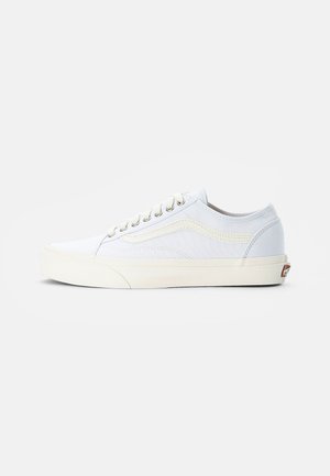 Baskets basses blanches avec semelle crème, lacets sur le devant et détail subtil d’une bande latérale, montrées de profil sur fond uni.