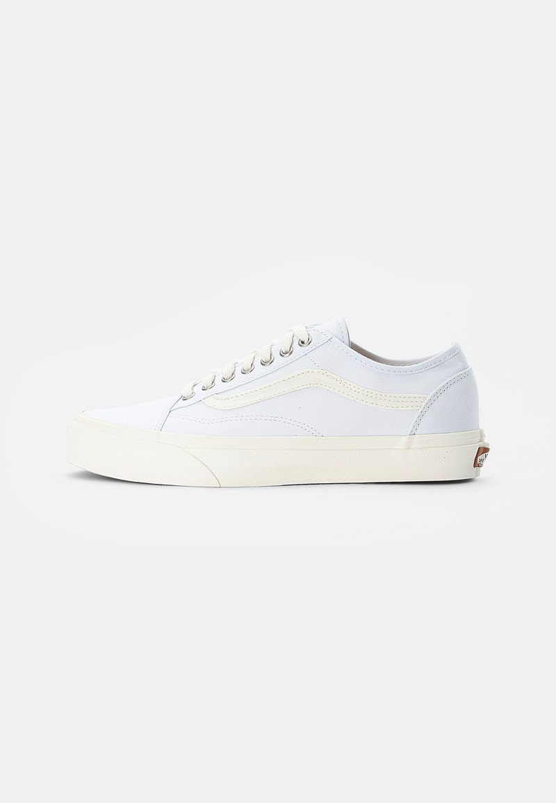 Baskets basses blanches avec semelle crème, lacets sur le devant et détail subtil d’une bande latérale, montrées de profil sur fond uni.