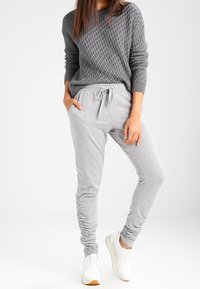 Pull gris en tricot avec un motif en losange, associé à un pantalon de jogging gris clair avec fronces et taille à cordon. Baskets blanches.