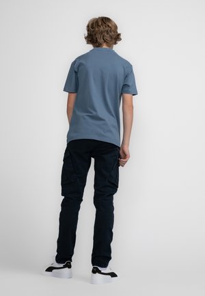 Niebieska bawełniana koszulka z krótkim rękawem, zestawiona z ciemnymi spodniami cargo. Noszona z białymi trampkami z czarnymi akcentami.