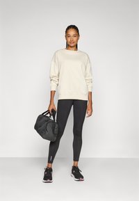 Beige huppari pitkillä hihoilla, mustat legginssit, mustat urheilukengät vaaleanpunaisilla yksityiskohdilla ja musta liikuntakassi. Yksinkertainen muotoilu ja istuva tyyli.