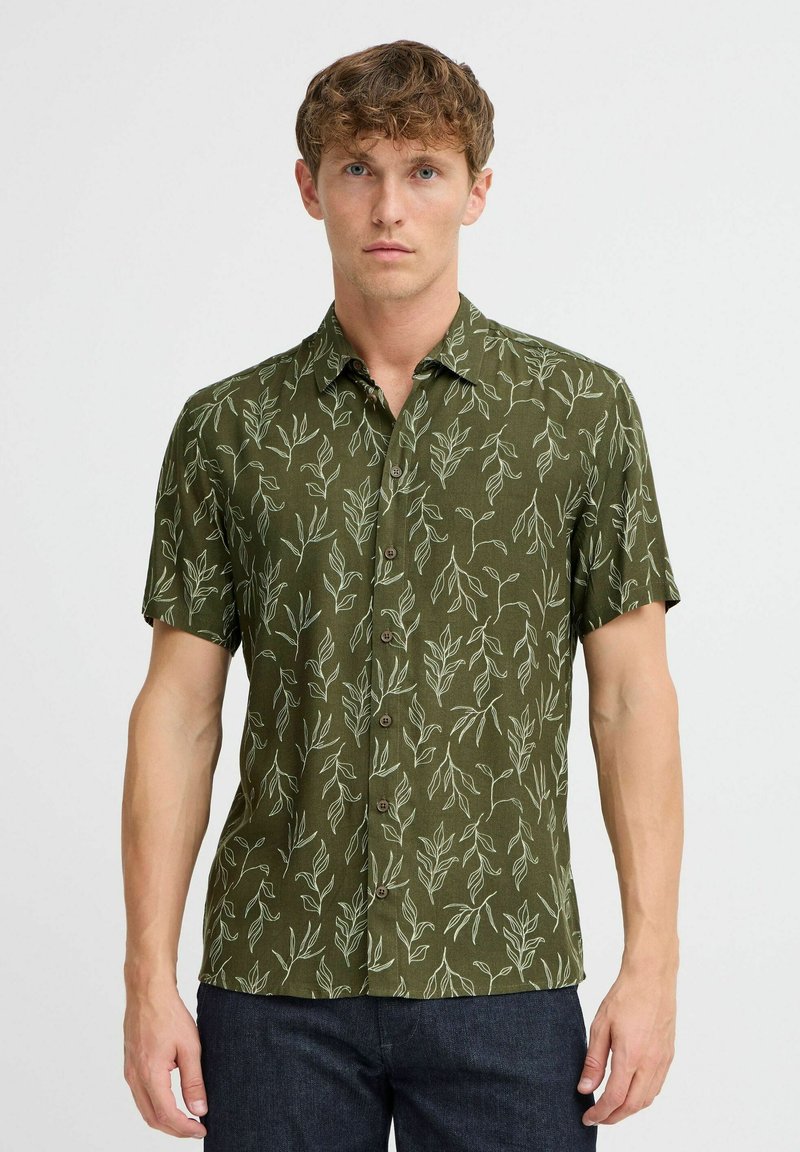 Camicia verde a maniche corte con motivo a foglie in verde chiaro. Presenta un'apertura frontale con bottoni e un colletto, realizzata in tessuto leggero.