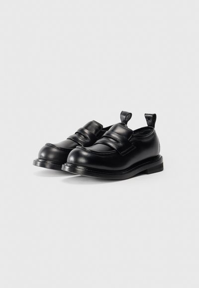 Svarta läderloafers med rund tå, med en sömdesign och två breda remmar över toppen. Strukturerad, minimalistisk stil.