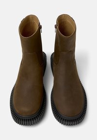 Botas tobilleras marrones con un acabado de cuero liso, cierres de cremallera y suelas de goma texturizadas, mostradas desde arriba sobre un fondo claro.