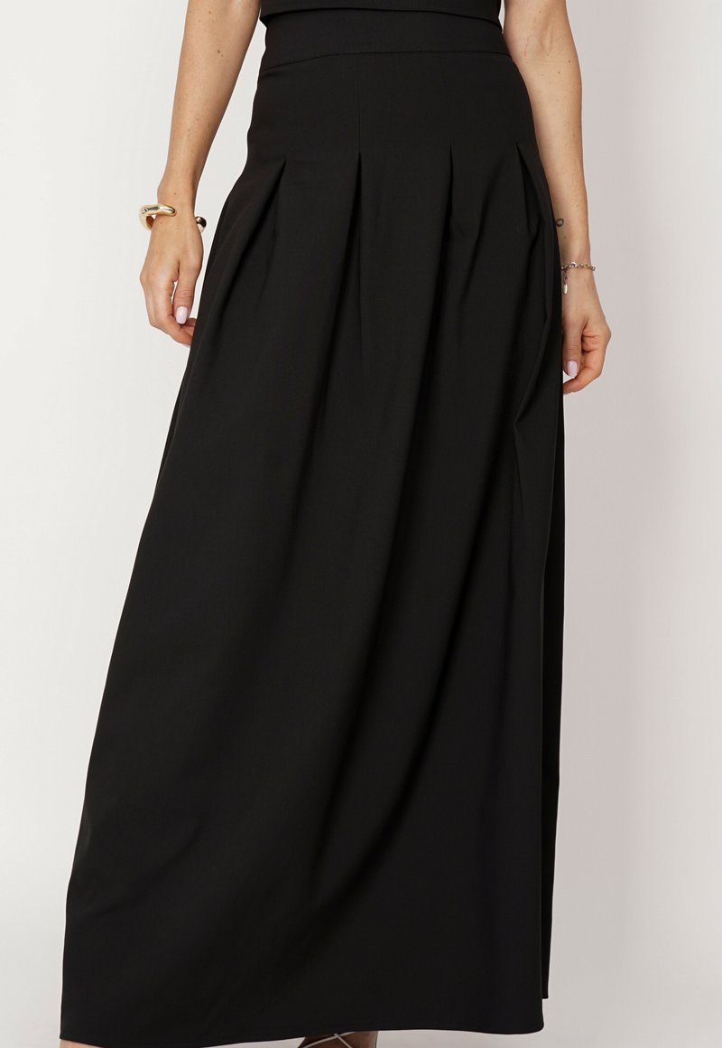 Czarna długa spódnica z lekkiego materiału, z bocznymi plisami i dopasowanym pasem. Gładka faktura o długości do ziemi.