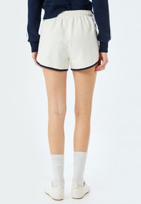 Pantaloni sportivi bianchi con bordo nero, dotati di una vita elastica. Indossati con calze bianche a coste e scarpe leggere. Tessuto di trama liscia.