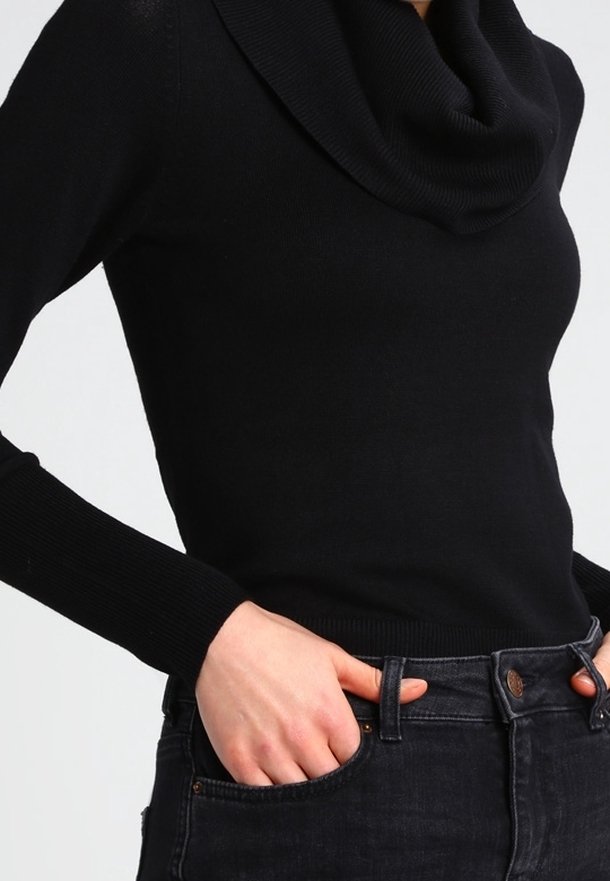 Pull noir avec un col bénitier, manches longues ajustées et poignets côtelés. Porté avec un jean foncé, mettant en valeur la texture lisse du tricot.