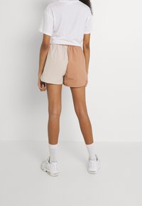 Beige ja hiekanväriset väriblokkihousut, joissa on joustava vyötärönauha. Valmistettu kevyestä kankaasta, pituus polven yläpuolella, yhdistetty valkoisiin nilkkasukkiin ja lenkkareihin.