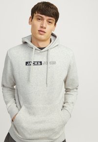 Világosszürke kapucnis pulóver pamut keverékből, elülső zsebbel és húzózsinórokkal. A "JACK & JONES" logó sötétkék színben látható.