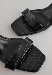 Schwarze flache Sandalen mit einem strukturierten Krokodilmuster an den Riemen und einem eleganten, quadratischen Zehendesign, mit einer glatten Oberfläche und minimalistischem Stil.