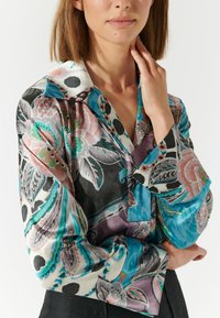Blusa di seta floreale con un motivo colorato che presenta tonalità di rosa, teal e nero. Ha un colletto e maniche lunghe con una texture liscia.