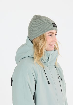 Grå ribbet strikbeanie med et logo-patch, båret med en lyseblå jakke med hætte og justerbare snore, der har en glat tekstur.