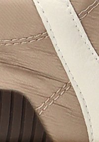 Zapatilla marrón claro con acentos blancos, que presenta una tela texturizada y costuras en contraste. La suela tiene un diseño estriado para mayor agarre.