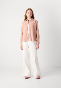 Light pink button-up shirt with long sleeves, paired with white wide-leg pants and pink shoes, set against a plain background.