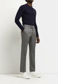 Polo shirt à manches longues bleu marine associé à un pantalon tailleur gris clair et des baskets blanches. Le polo présente un col et une texture subtile.