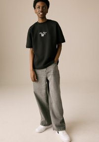 Black cotton t-shirt with "New York 92" printed in white; loose-fit grey denim pants; white sneakers with perforated design.