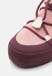 Mauve sportssko med overdel i semsket skinn og gummi, teksturert såle, elastiske lisser og hvit detalj nær snøringen for sikker passform.