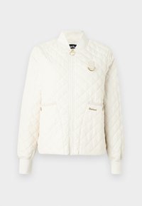 Gestepptes cremefarbenes Jäckchen mit geripptem Kragen, Reißverschluss und zwei Fronttaschen. Mit goldfarbenen Hardware-Accents und subtilen Logodetails.
