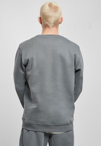 Felpa grigia con scollo tondo, polsini e orlo a coste, caratterizzata da una texture liscia e una vestibilità rilassata. Dettaglio di cuciture visibili lungo la spalla.