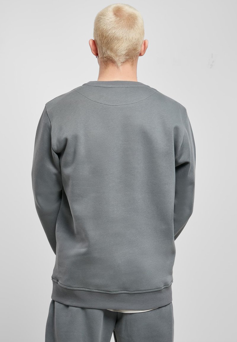 Felpa grigia con scollo tondo, polsini e orlo a coste, caratterizzata da una texture liscia e una vestibilità rilassata. Dettaglio di cuciture visibili lungo la spalla.