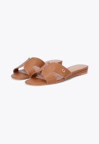 Brązowe syntetyczne klapki z odkrytymi palcami, z krzyżującymi się paskami, niskim obcasem i dekoracyjnym akcentem w postaci logo. Gładka faktura.