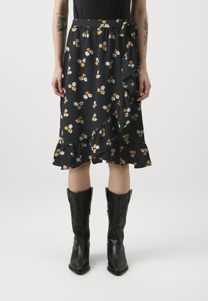 Jupe florale noire avec des fleurs jaunes et blanches, ourlet volanté et taille élastique. Associée à des bottes de cowboy noires.