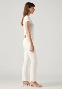 Witte slim-fit jeans gecombineerd met een kort mouwbloemtop. De outfit heeft een lichte textuur en een minimalistisch ontwerp met banden sandalen.
