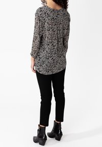 Blusa nera con motivo floreale in tessuto trasparente, maniche lunghe e collo rotondo, abbinata a pantaloni neri slim e stivaletti neri.