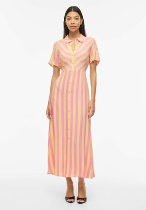 Kvinne iført en gul og rosa vertikal stripet midi-kjole med knapper, korte ermer og svarte åpne hæler.