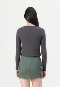 Krátky top s dlhým rukávom v tmavosivej farbe so svetlomodrým výstrihom; spárovaný s zelenou sukňou s vreckami a rozšíreným strihom.
