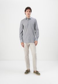 Light blue long-sleeve shirt with small geometric patterns, buttoned front, paired with beige trousers and green suede loafers.
