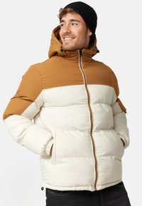 Padded jacket with a tan upper section and cream lower section, featuring a zip closure, hood, and side pockets. Fabric appears smooth and warm.