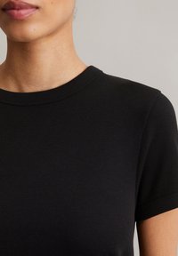 Schwarzes Kurzarm-T-Shirt aus geripptem Stoff, mit Rundhalsausschnitt und glatter Textur. Keine sichtbaren Grafiken oder Muster.