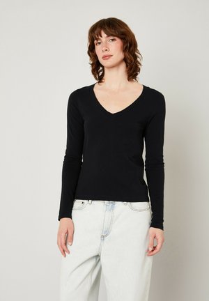 Černý dlouhý rukáv V-krk top vyrobený z hladké látky, přiléhavý na tělo. V kombinaci s světle modrými oversized džíny. Minimalistický design, bez vzorů.