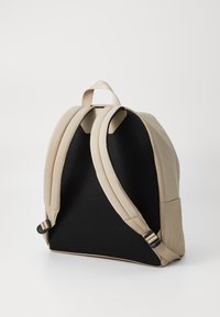 Zaino in tessuto beige con schienale in rete nera, spallacci imbottiti e fibbie regolabili. Presenta una forma arrotondata e cuciture senza soluzione di continuità.