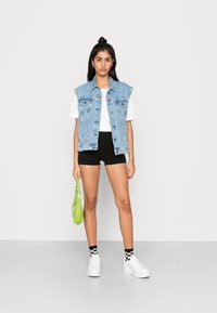 Denim ilmanhihaine takki, valkoinen t-paita, mustat shortsit, valkoiset korkeat tennarit, musta-valkoiset ruudulliset sukat, vihreä käsilaukku.