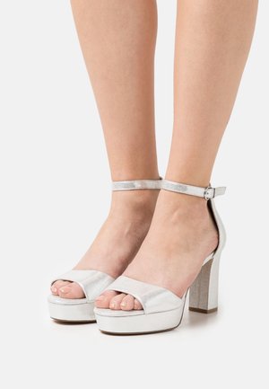 Zilveren hoge platform sandalen met open tenen en enkelbandje. Glanzende metallic afwerking en textuurzool.