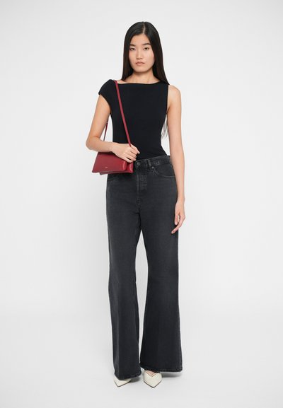 Sort ærmeløs top, højtaljede, vide mørke denimjeans og en rød læder crossbody taske. Modellen bærer spidse hvide hæle.