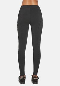 Tylny widok osoby w wysokich czarnych legginsach z delikatnymi detalami bocznych paneli oraz czarnych błyszczących trampkach.