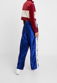 Kroppad kavaj i sammet röd och vit, kombinerad med blå satinbyxor med vita sidremsor och tryckknappdetaljer, bärs med vita sneakers.