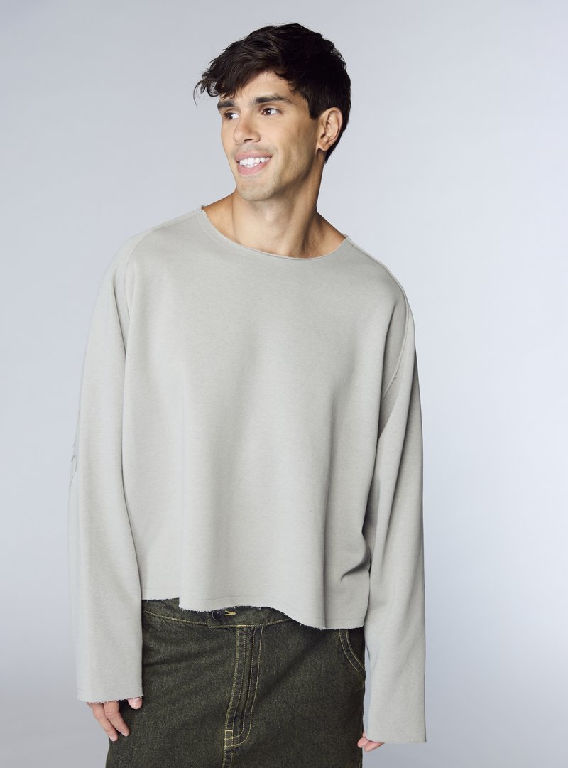 Felpa grigio chiaro a maniche lunghe con scollo ampio, design corto e tessuto morbido, abbinata a una gonna di denim verde scuro con cuciture visibili.