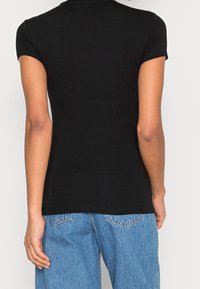 Schwarzes, figurbetontes T-Shirt mit kurzen Ärmeln und Rundhalsausschnitt, kombiniert mit hellblauen, hochgeschnittenen Jeans, was einen lässigen Look zeigt.