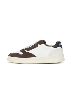 Baskets basses en cuir blanc avec panneaux en daim marron, lacets blancs, semelle en caoutchouc crème, et languette de talon noire avec logo de la marque.