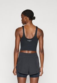 Svart atletisk croptop med breda band, ribbad struktur och logodetalj. Matchas med svarta shorts och spandex under.