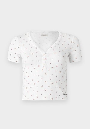 Blusa blanca de manga corta con pequeño estampado floral multicolor, escote en V con tres botones y sutiles rayas verticales texturizadas.