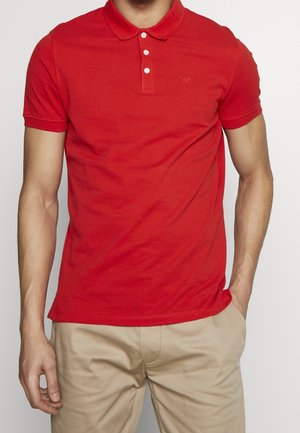 Red polo shirt with three-button placket, short sleeves, and a small logo on the chest. Fabric appears smooth and lightweight.