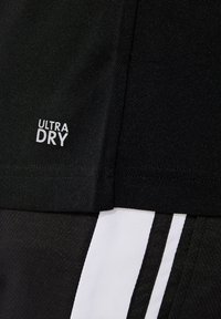 Černé sportovní šortky s bílým logem "ULTRA DRY". Mají texturovanou látku a kontrastní bílé pruhy po stranách.