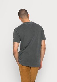 Mörkgrå T-shirt med en avslappnad passform, korta ärmar och en V-formad sömdetalj på baksidan. Mjuk, texturerad bomullsmaterial.