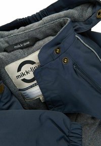 Chaqueta exterior azul marino con un suave forro polar gris, que presenta una cremallera, detalles de botones y una etiqueta que indica la marca y las instrucciones de cuidado.