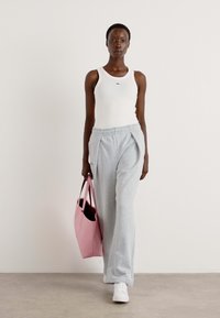 Grå joggebukser og en hvit tanktopp, kombinert med en rosa totebag. Buksene har en avslappet passform og plisserte detaljer; vesken har en glatt tekstur.